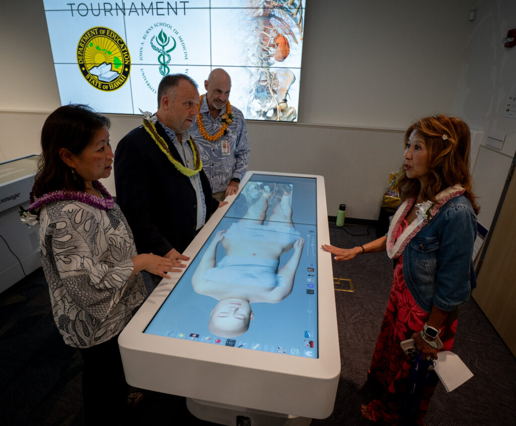 La Primera Dama Jaime Green y el gobernador Josh Green hablan con la Dra. Jaimie Tom durante una sesión educativa que presenta una mesa de autopsia virtual creada por Anatomage de Santa Clara, California, en JABSOM el 7 de abril de 2026. La escuela de medicina Sam Shomaker observa. (Craig Fujii/Civil Beat/2026)