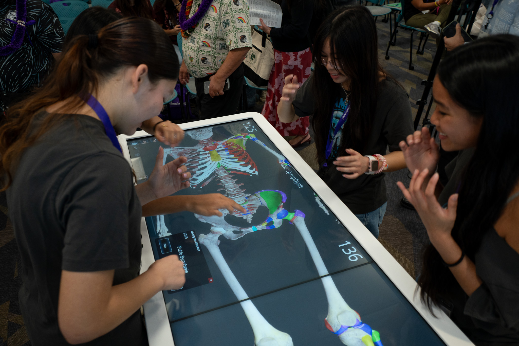 Los estudiantes de Kapolei High School trabajan con la mesa de autopsia virtual Anatomage en JABSOM el 7 de abril de 2026. De izquierda a derecha están Anna Steed, Benyapa Martin y Emani Villegas. Faith Antonio es el cuarto miembro del equipo que no aparece en la foto. (Craig Fujii/Civil Beat/2026)
